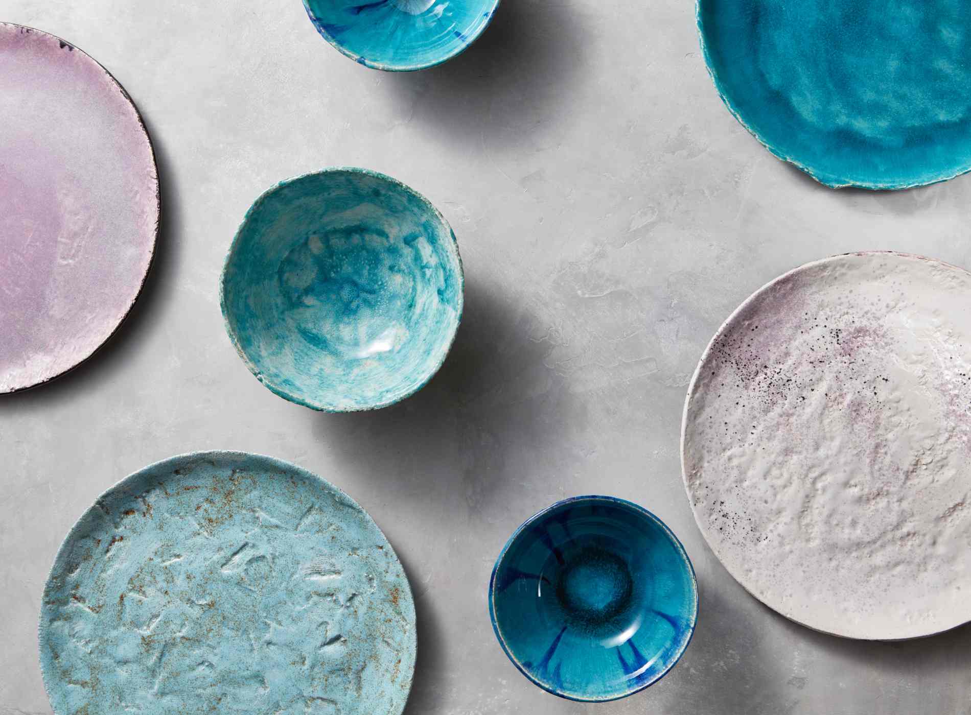 Ceramic bowls of different colors, sizes and types are empty on a gray concrete background. Flat lay of porcelain dishes handmade.