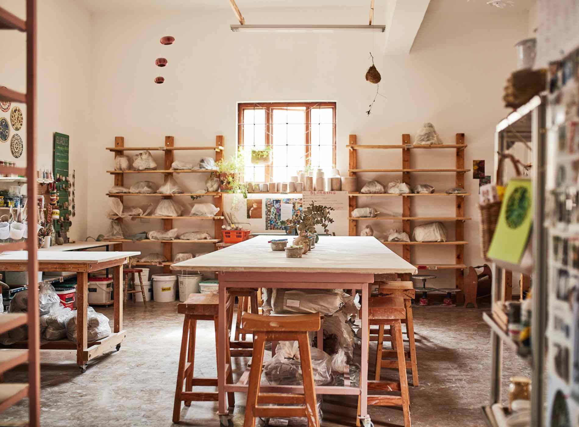 An empty clay pottery store or workshop with a potter's desk and handmade craft collection on a shelf in an empty shop during the day. Craftsman workplace with ceramic pots, plates and jars on a rack