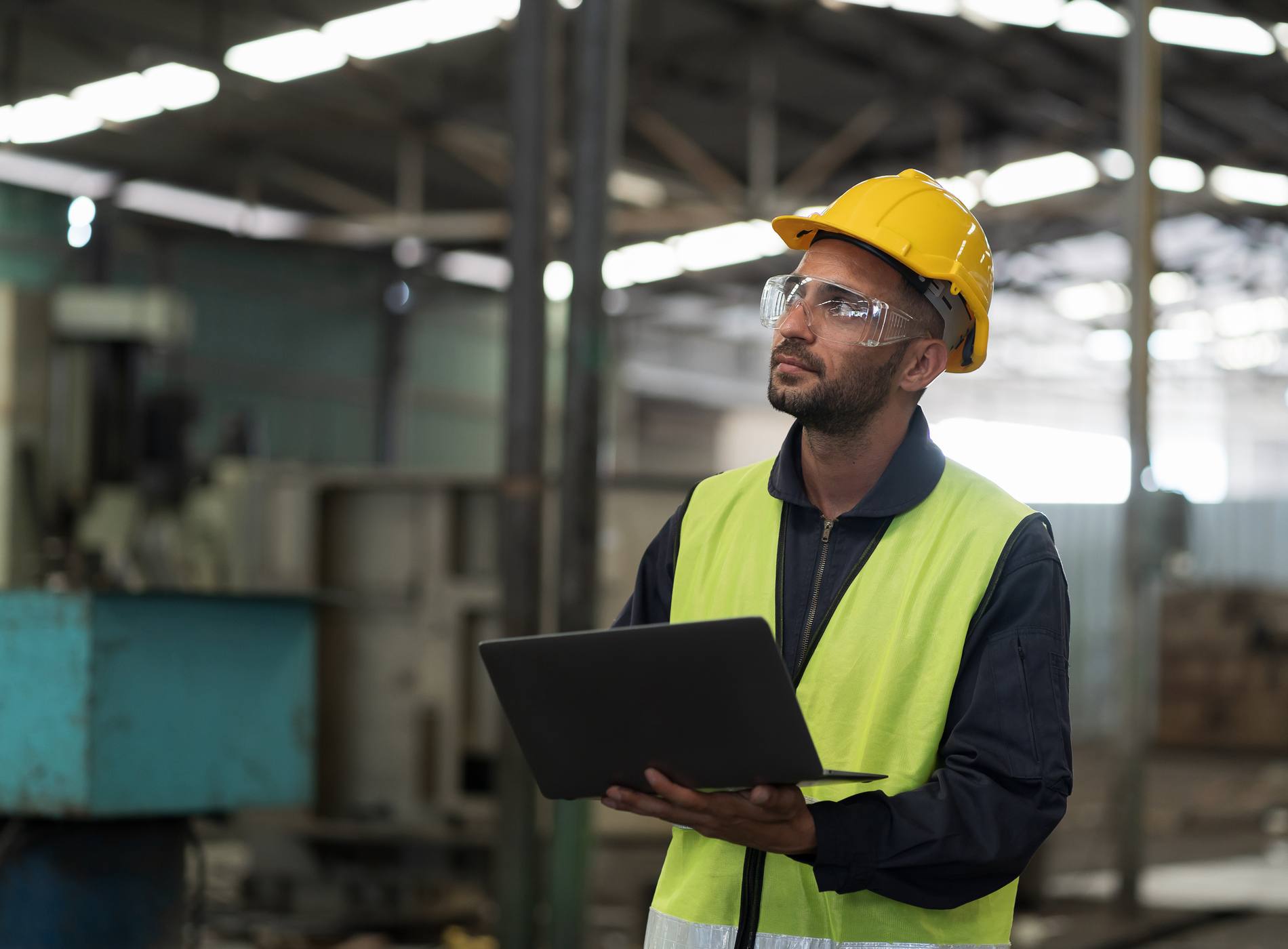 Male engineer worker working with clipboard and control machine in factory. Male worker working with CNC machine with safety uniform, helmet in industry factory