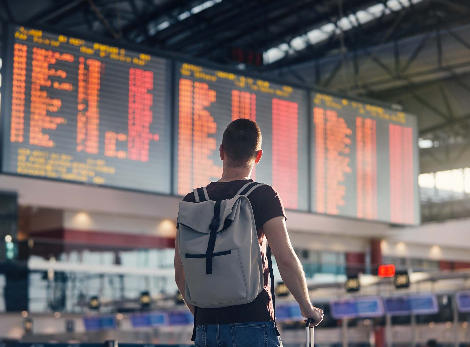 Traveling by airplane. Man walking with backpack and suitcase walking through airport terminal and looking at departure information.