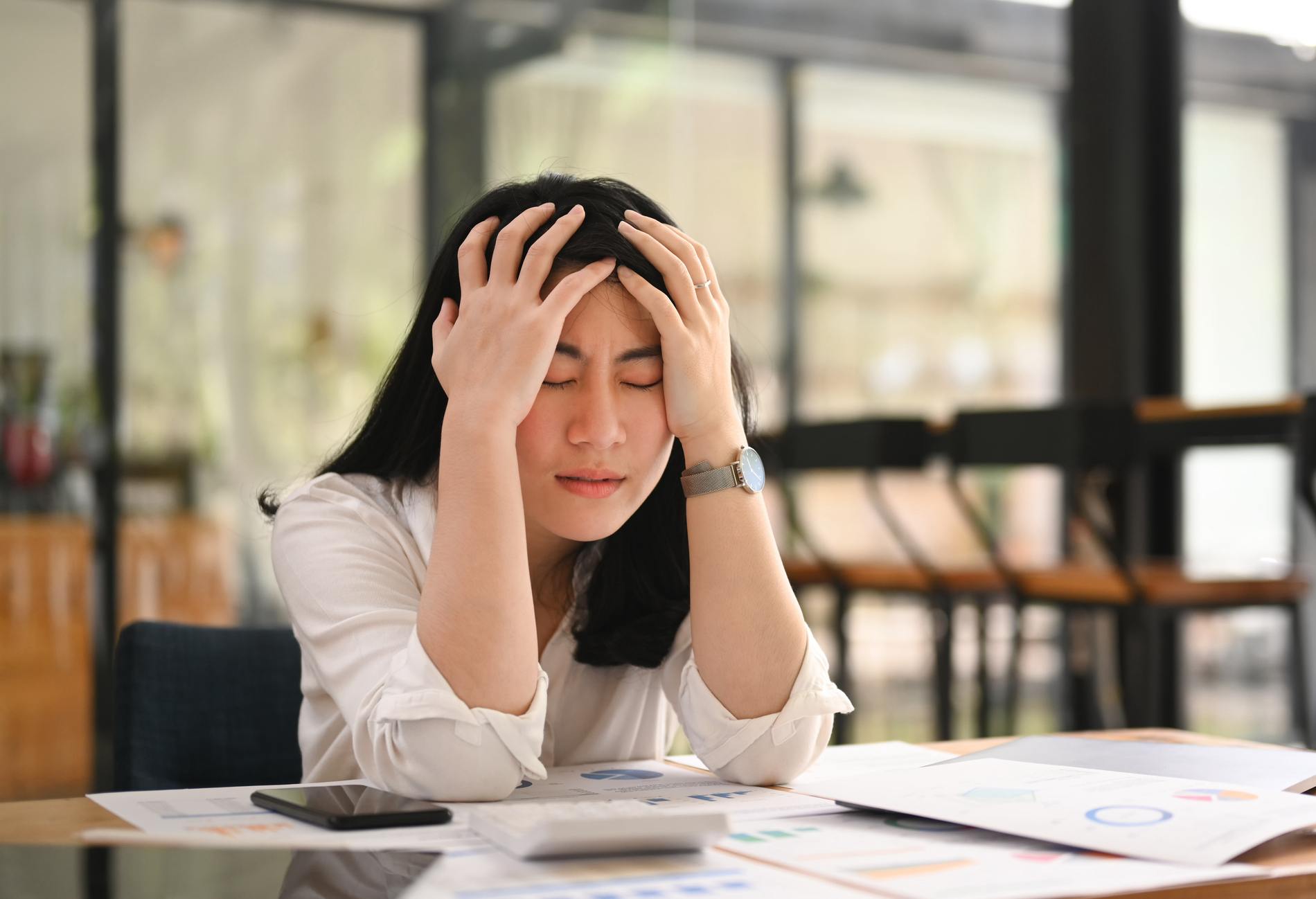Tired office worker holding her head, feeling strong headache, exhausted from overwork or stress at work.