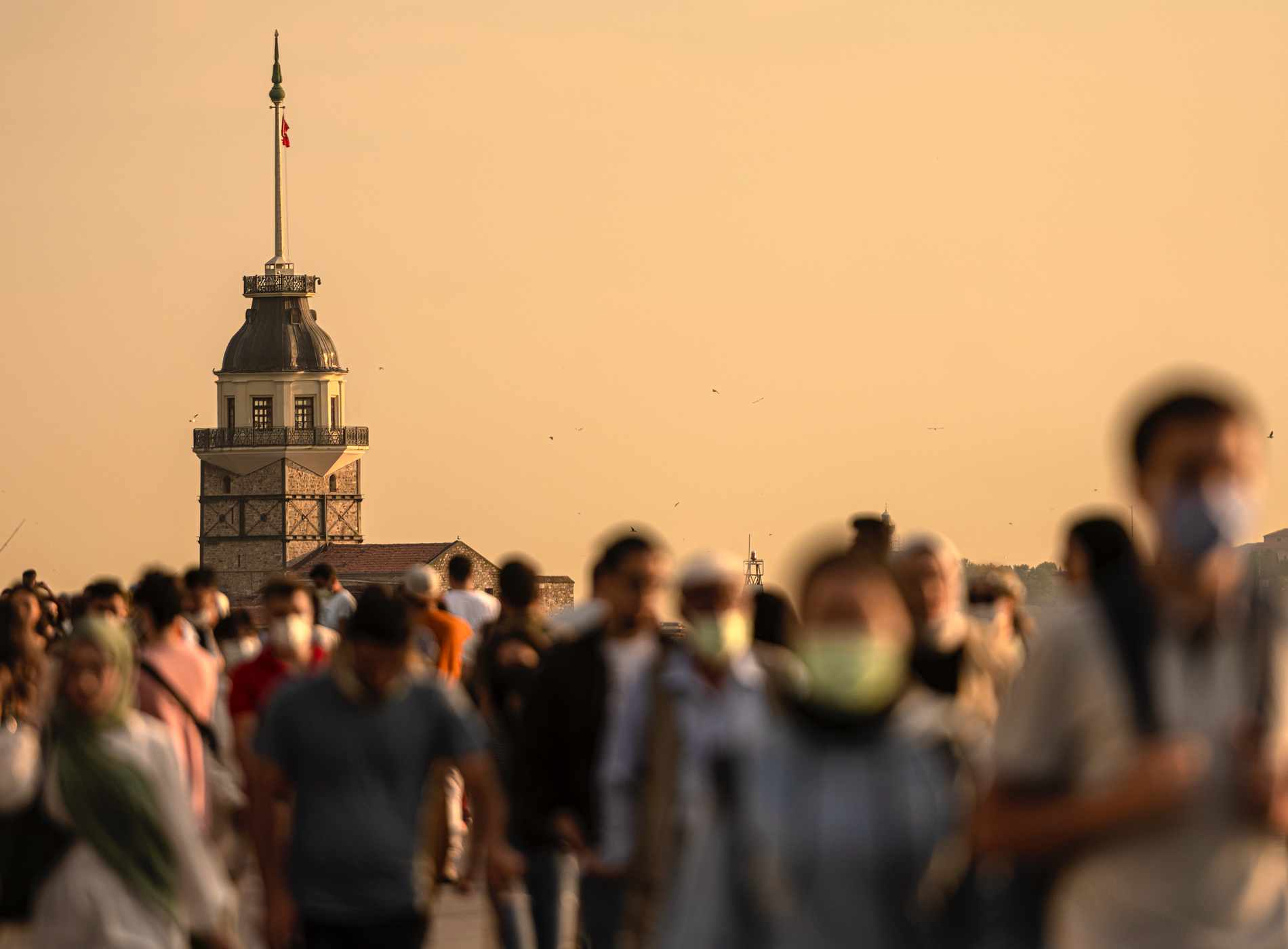 Crowd of people on the Üsküdar beach in Istanbul. The historical Maiden's Tower is visible in the background. Unrecognizable people due to narrow depth of field.