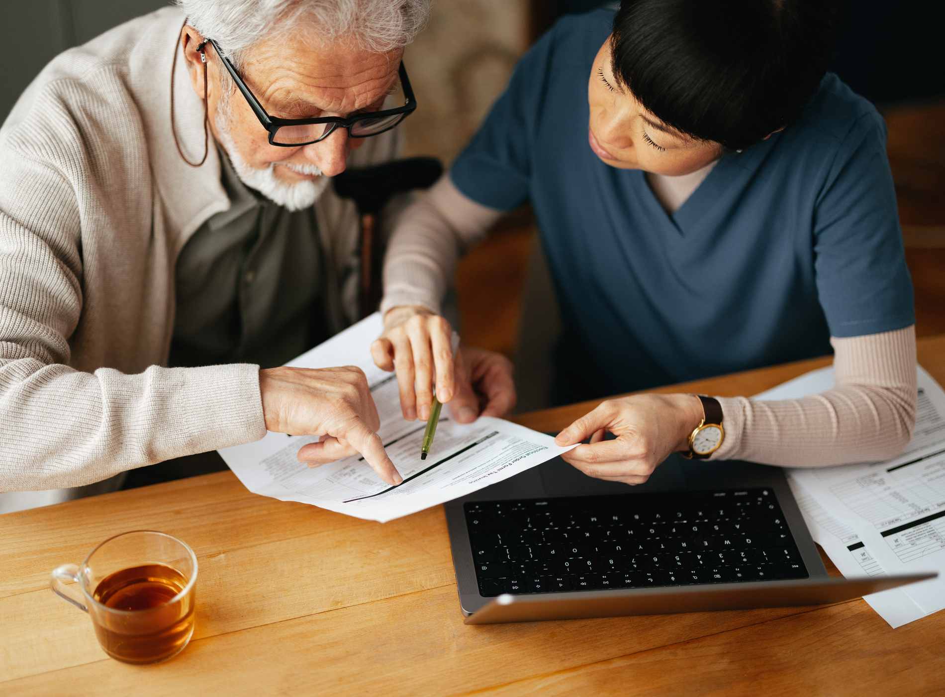 High angle view of a Japanese female caregiver doing home finance online on a computer together with her worried elderly patient at his home.