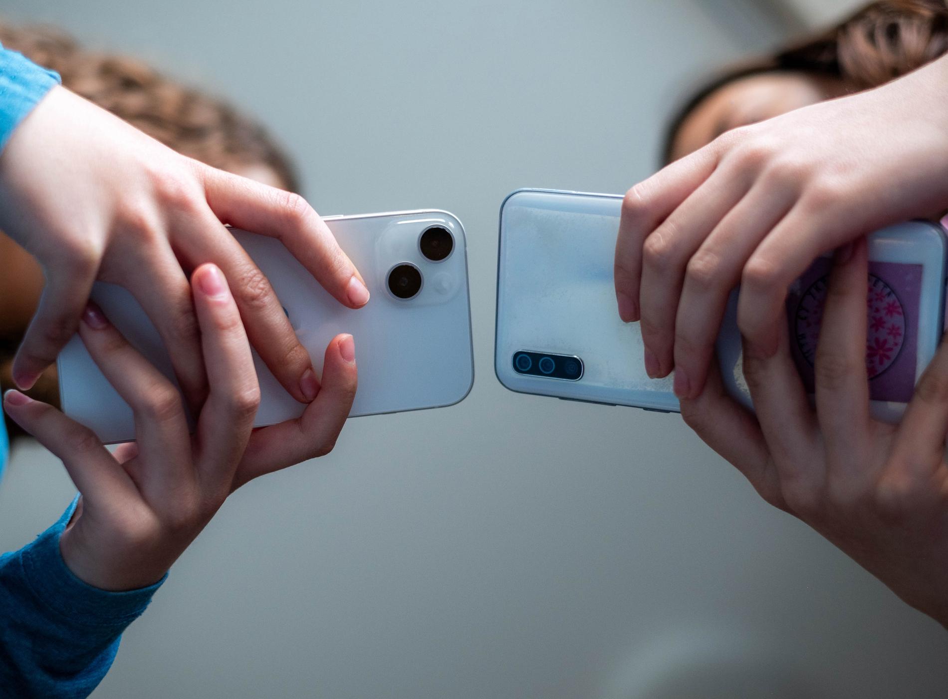 close up hands of two girls holding mobile phones and exchanging pictures