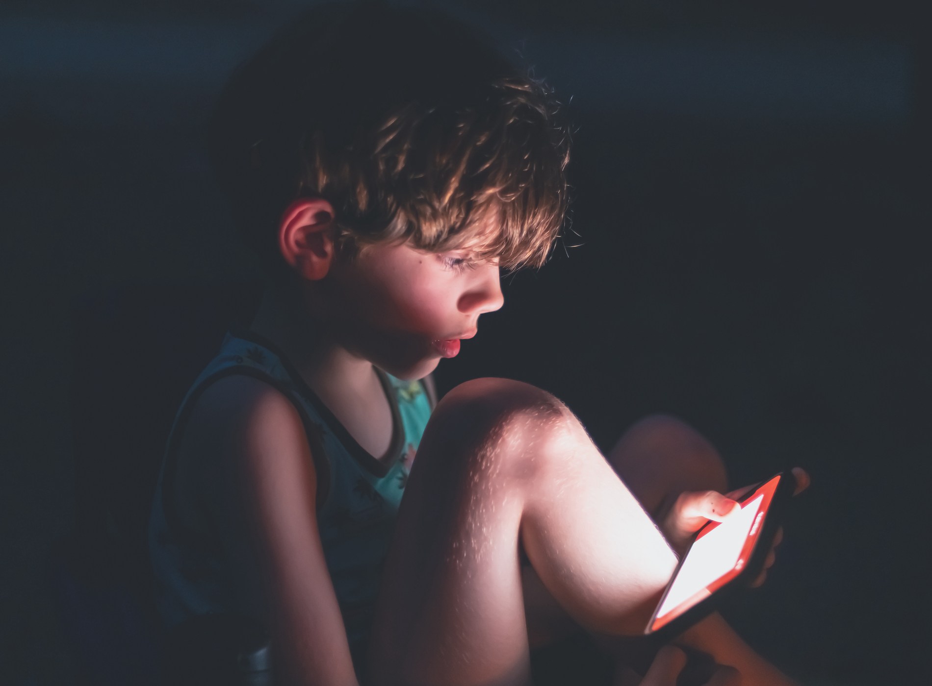 A boy reads a story on a smart phone by a campfire.