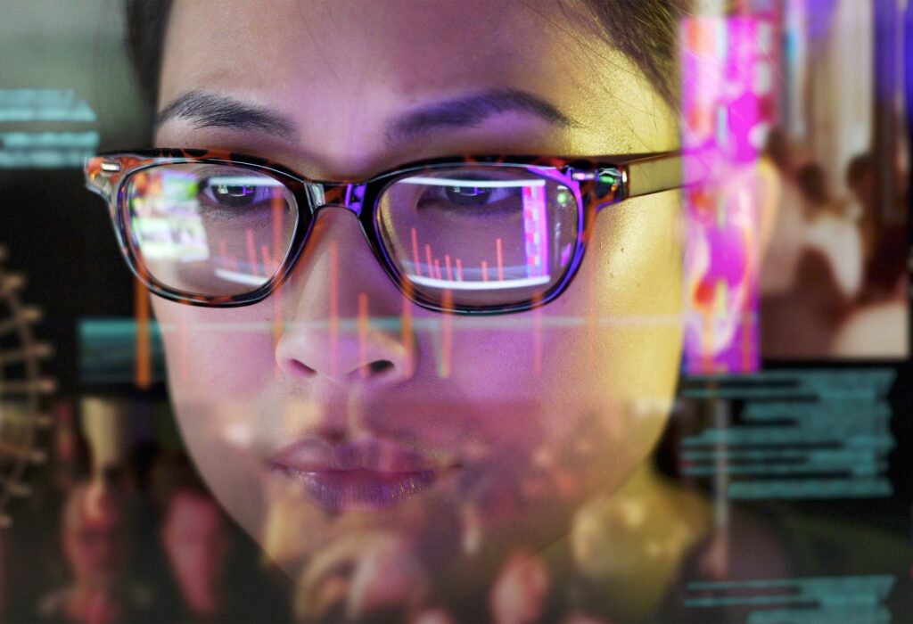 Close up stock photo of an Asian woman carefully studying moving data on her computer screen, the screen is unusual as it is transparent and the camera is looking through the back of the screen.