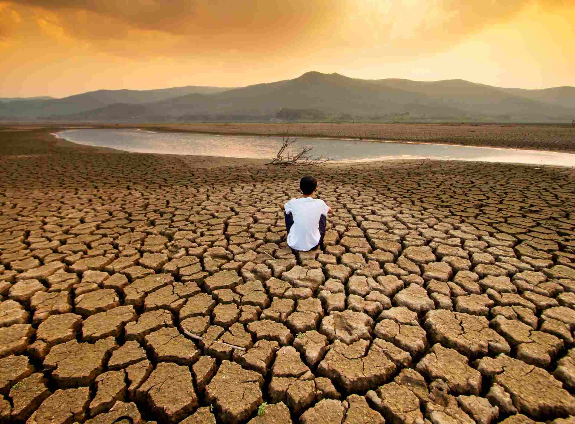 Climate change and global warming concept. Children sitting on drying lake with the sky turning orange by an pollution from industrial or city.