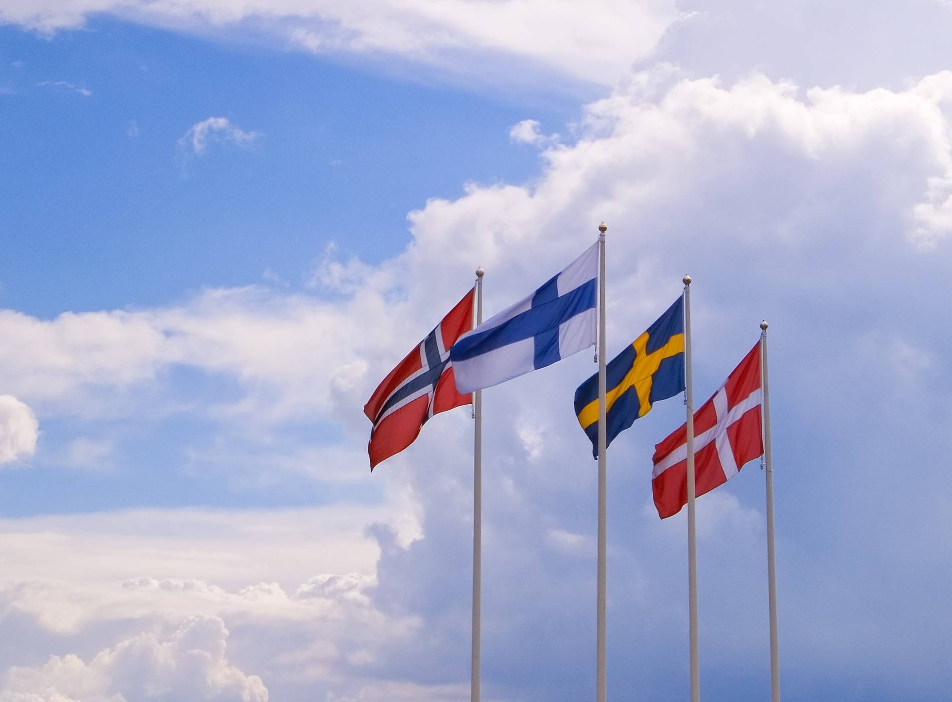 "flags of the nordic (scandinavian) countries of (left to right) norway, finland, sweden and denmark against a dramatic sky."