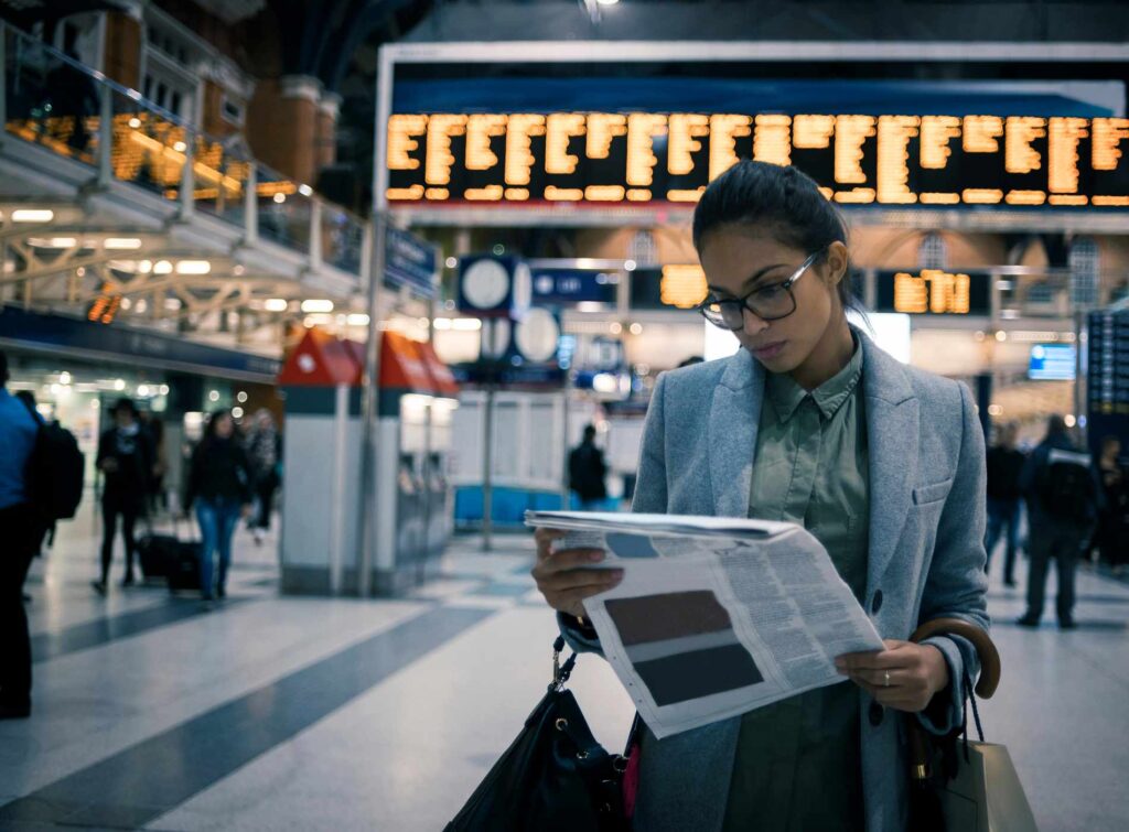 businesswoman reading newspaper while waiting for her train at the station