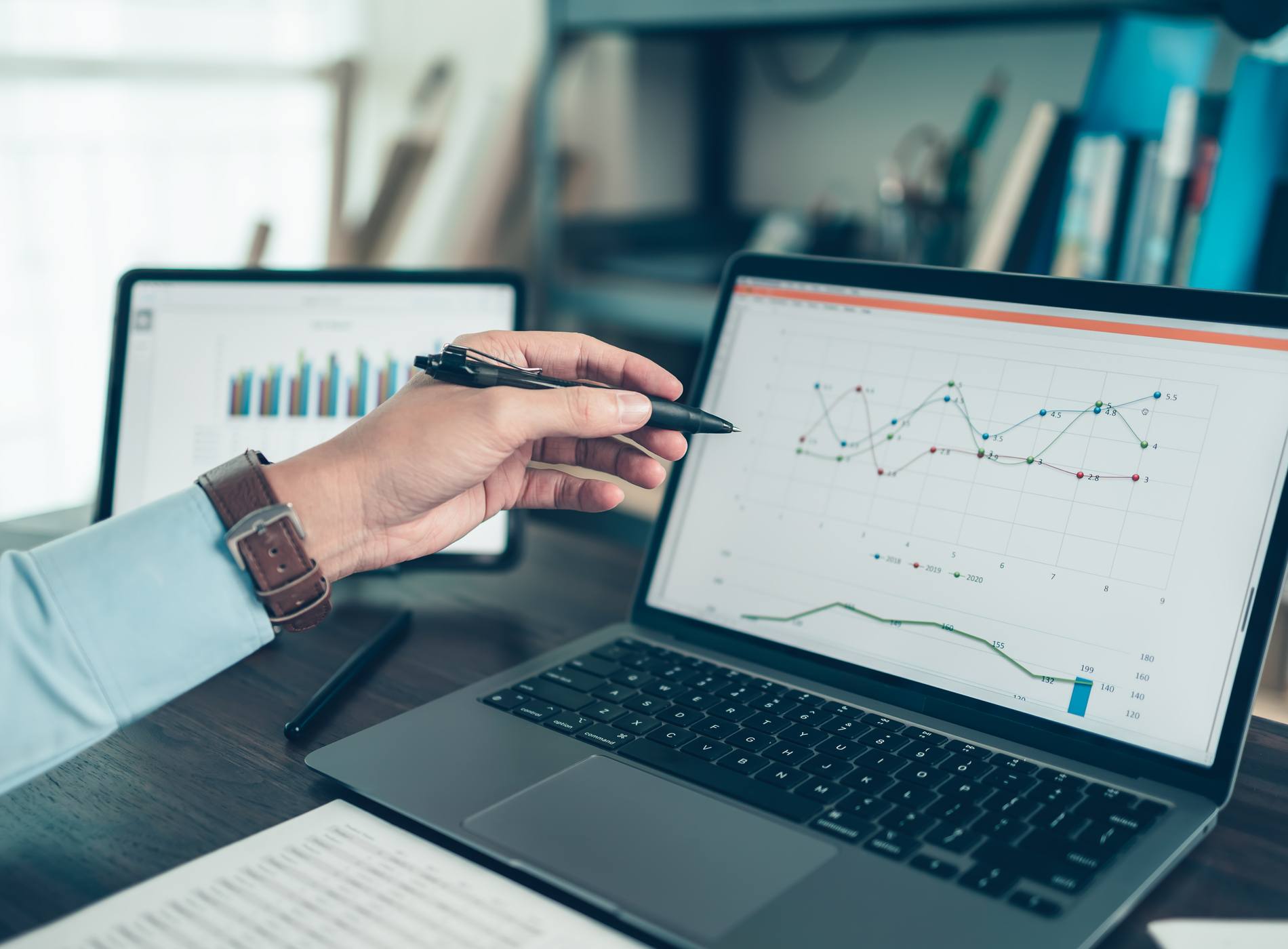 Business man hold stylus pen and pointing to laptop at office with document report, graph, financial report on screen.