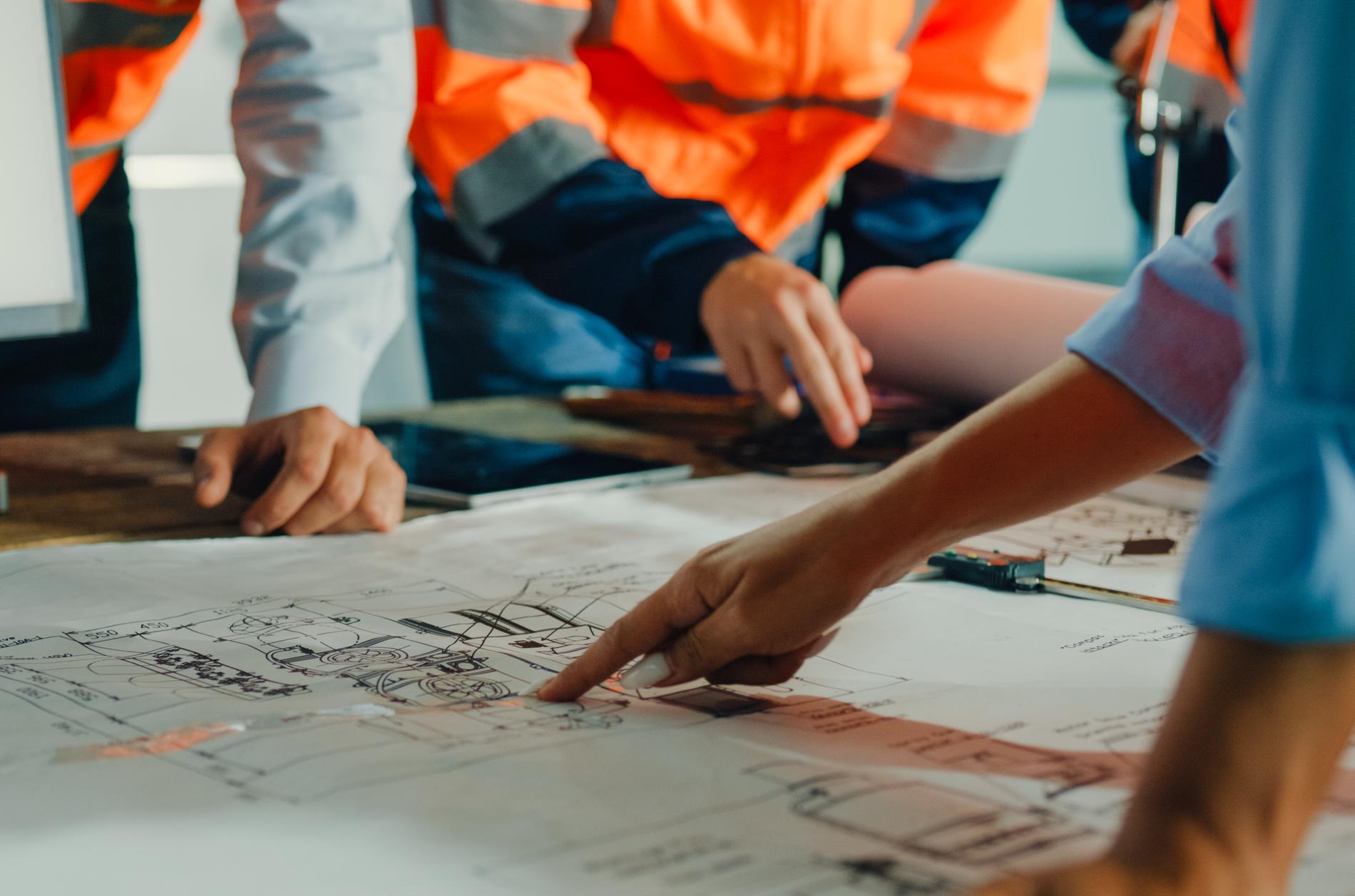 Closeup of team of industrial engineers meeting analyze machinery blueprints consult project on table in manufacturing factory. Working in manufacturing plant or production plant concept.