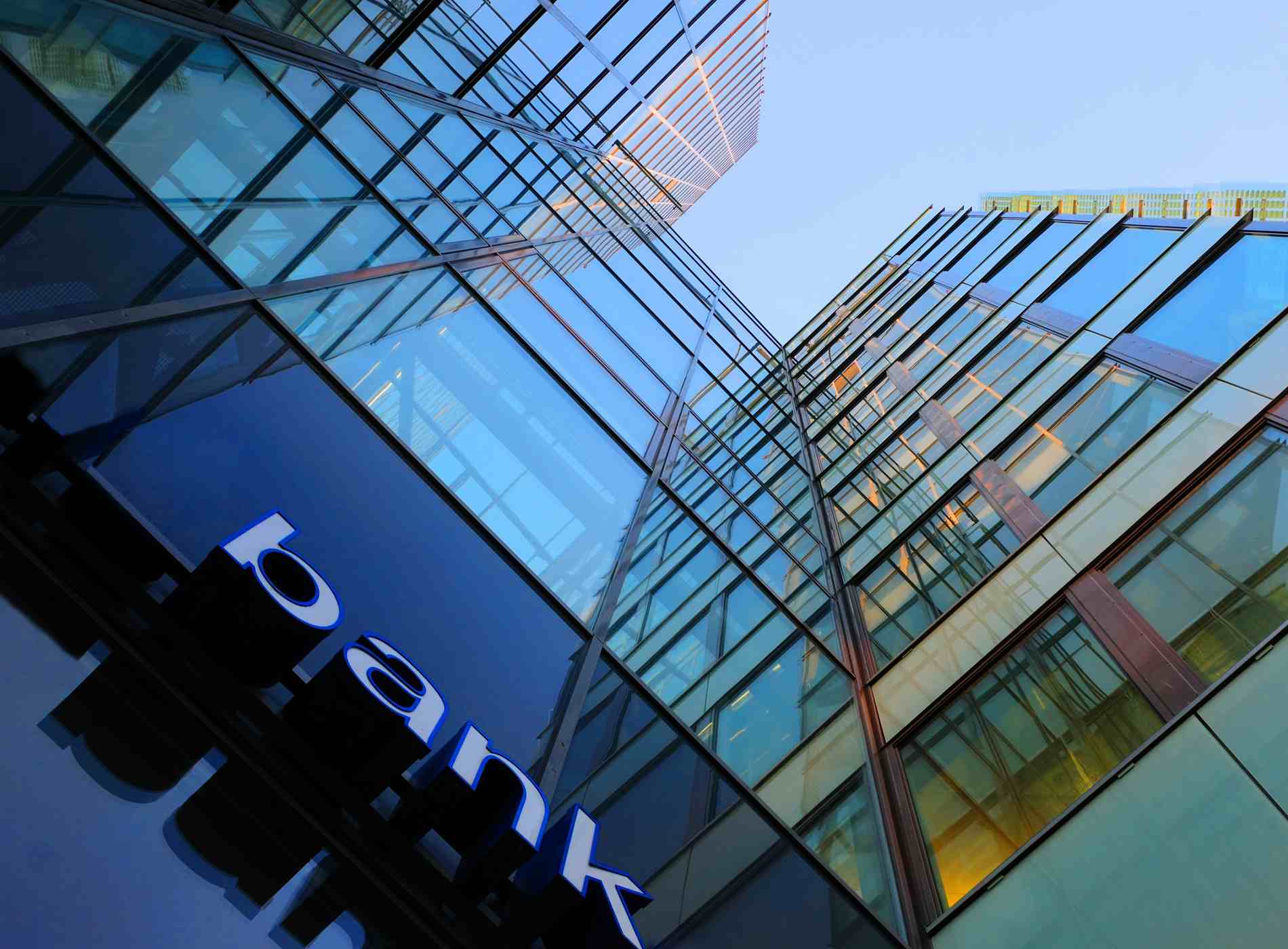 Bank corporate finance building seen from below. The sign "bank" visible close. Sky reflecting in the glass facade. More Facade pictures below