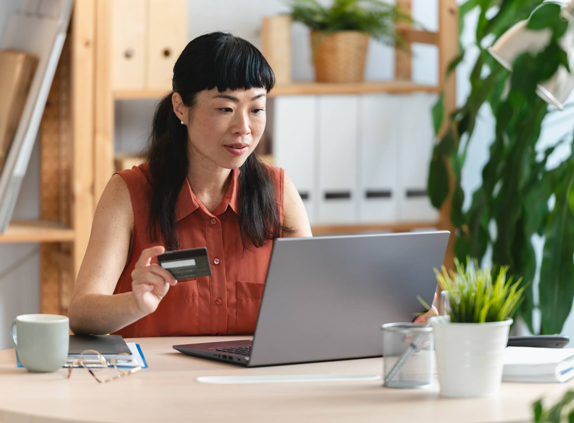 Small business entrepreneur sitting at desk with laptop, holding credit card and making online payment or managing finances in modern workspace