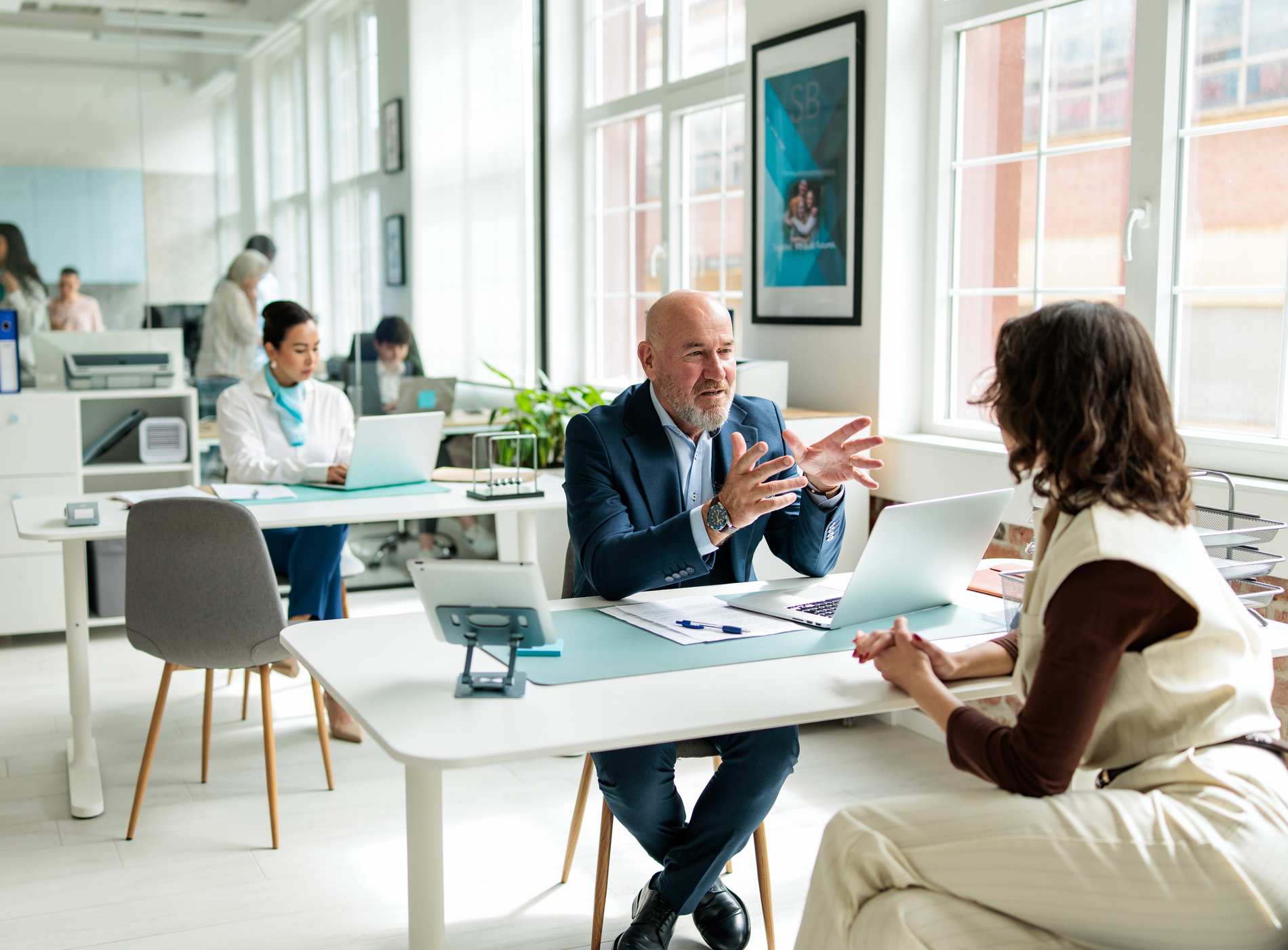 Experienced financial advisor providing guidance to a female customer while seated at his desk in a modern bank office.