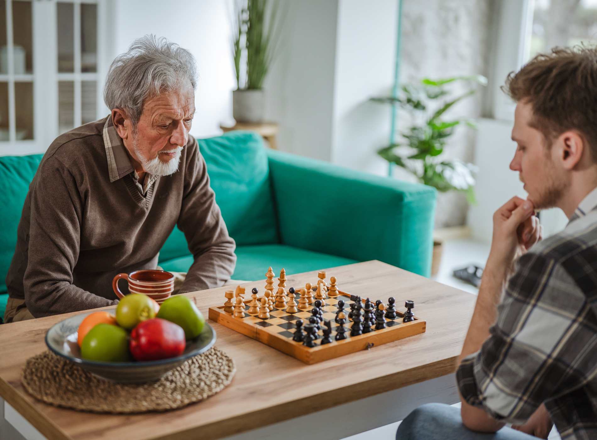 Senior man and young man engaging in a strategic game of chess at home, enjoying leisure time and inter generational bonding while concentrating on their next moves