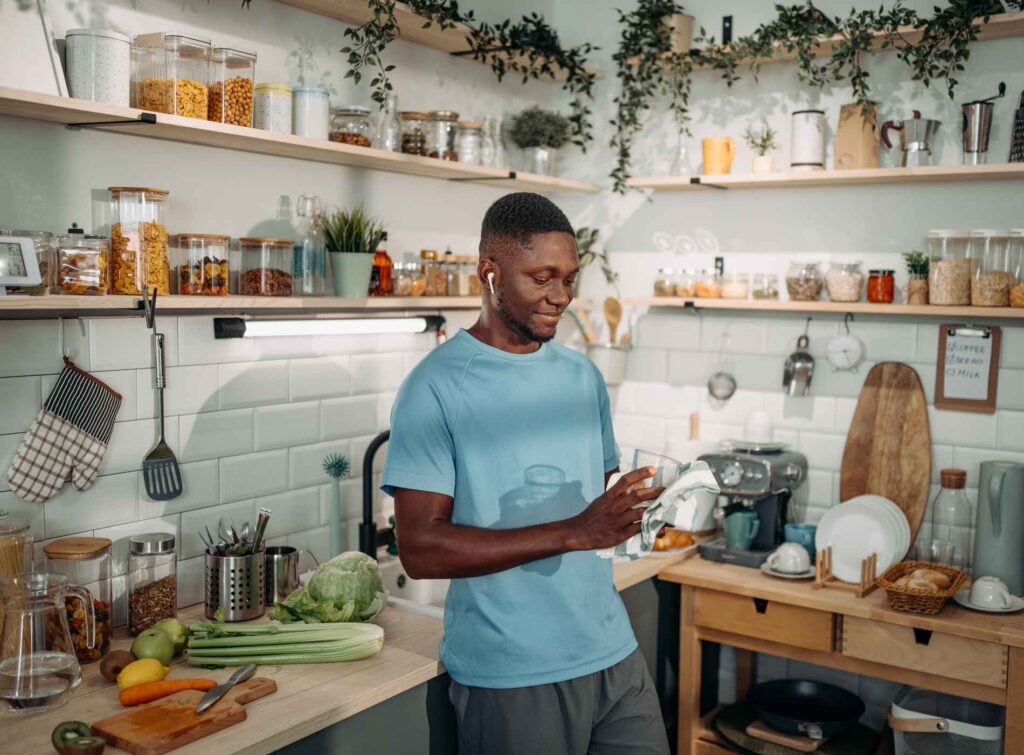Young man in sport's clothes cleaning glass for smoothie in a domestic kitchen at home