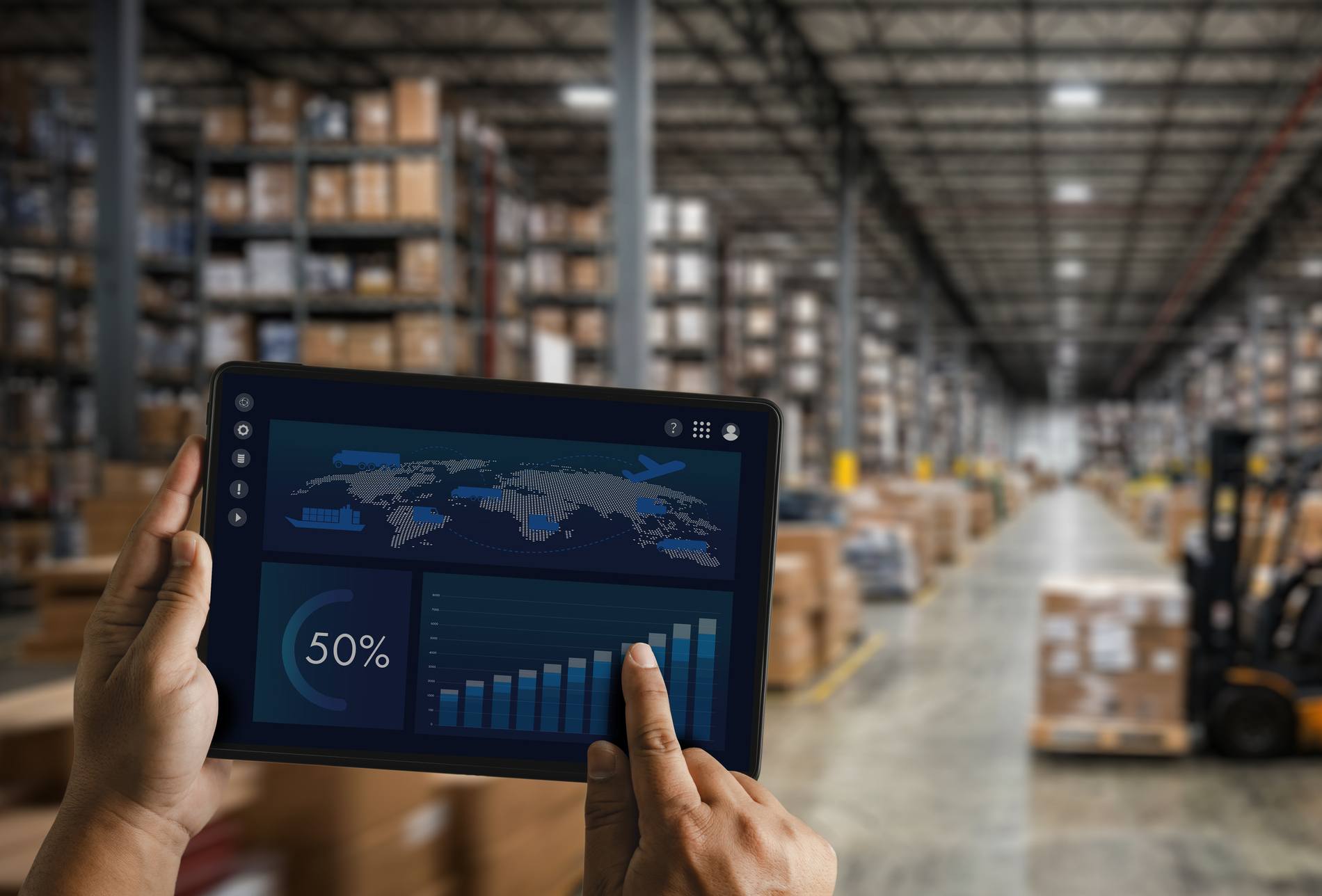 Hands holding tablet with warehouse dashboard and logistics charts inside storage facility, supporting inventory monitoring, supply chain analysis, distribution management, and warehouse workflow.