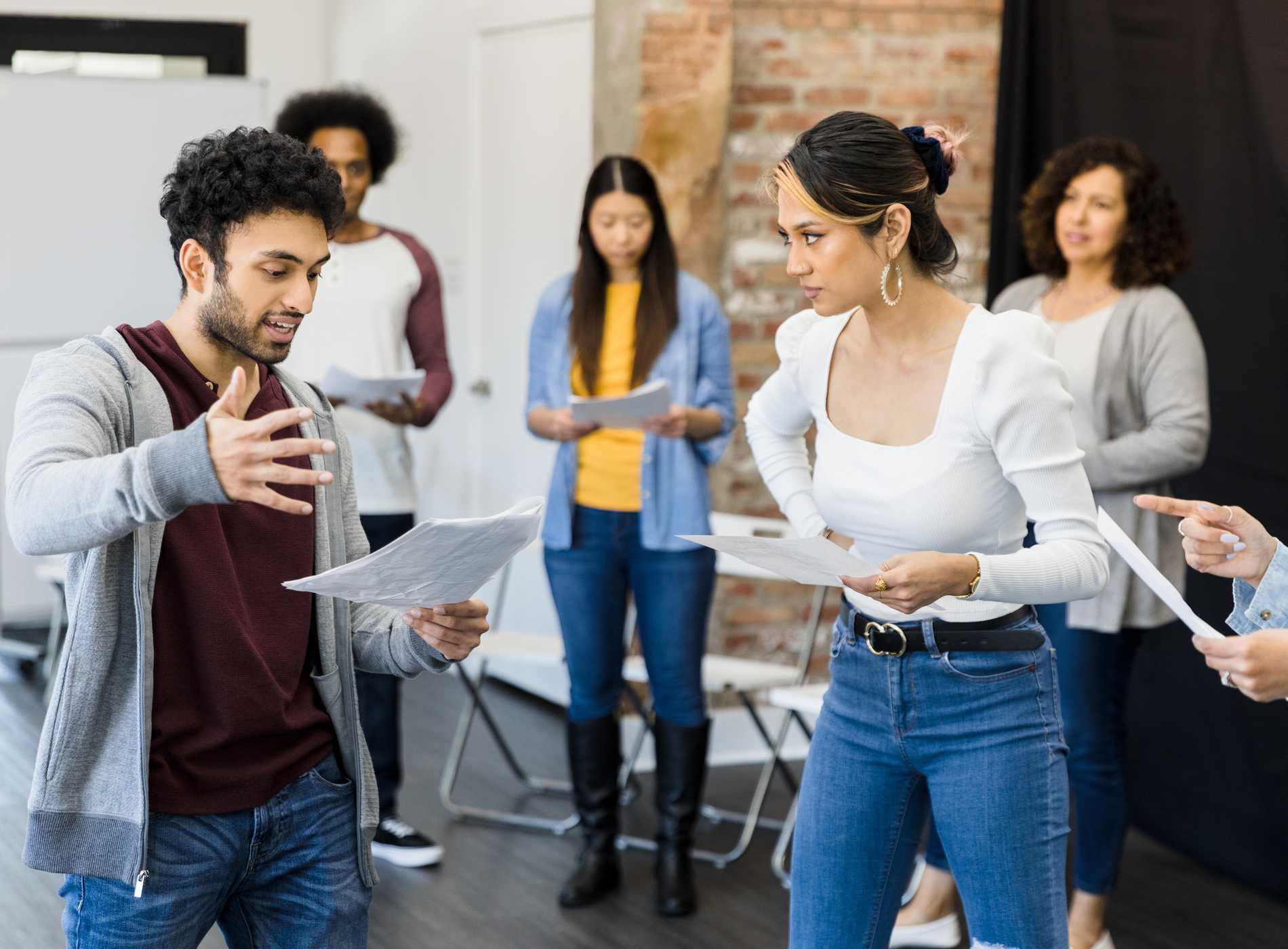 The multiracial group of actors practice the play in the studio. They each read from a script.